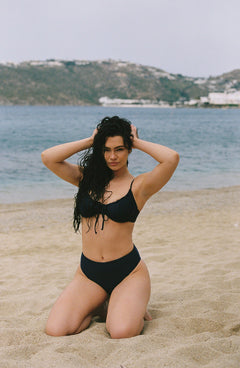 Indigo drawstring top with front tie detail, shown on model kneeling on sandy beach, ocean backdrop, lifestyle view